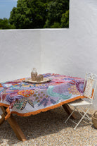 Colorful embroidered tablecloth on a wooden table with a white wall and greenery in the background