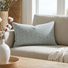 A textured light blue throw pillow resting on a beige upholstered sofa in a bright, modern living room setting.
