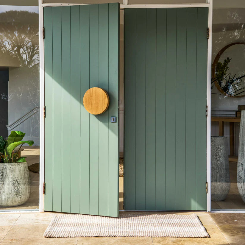 Green wooden door with a circular wooden handle in an outdoor setting