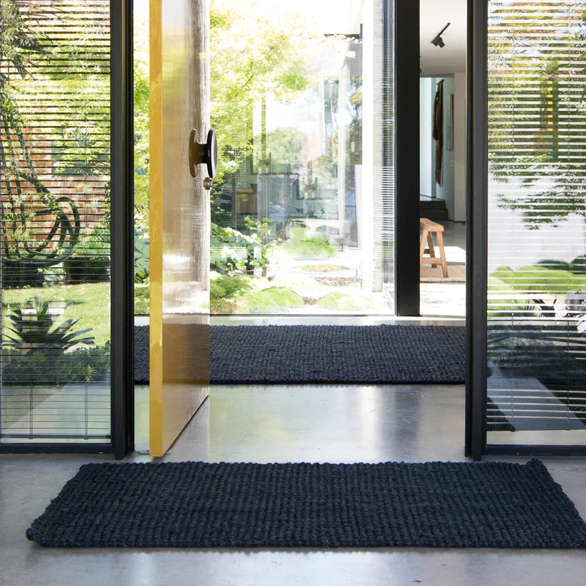 Black doormat in front of a glass door with a view of greenery outside