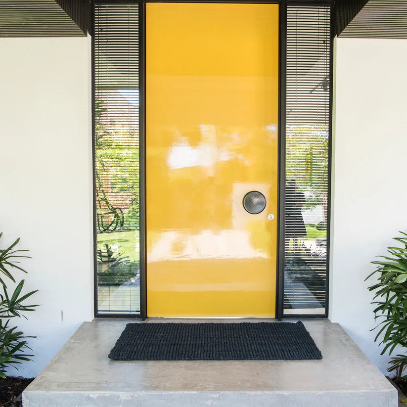 Yellow door with glass panels on a white wall, featuring a doormat.