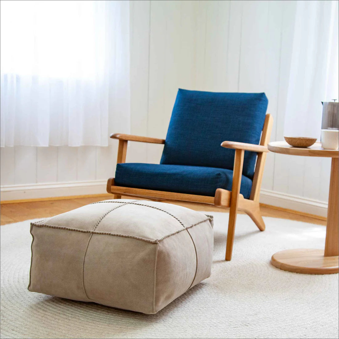 Blue armchair with wooden frame and beige ottoman in a room with white walls and wooden floor.