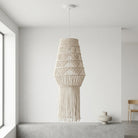 A cream macrame pendant light hanging in a minimalist, bright white room with a concrete ledge and a small ceramic vase.