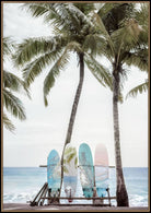 A framed art print depicting a tropical beach scene with three palm trees, ocean waves, and three colorful surfboards resting on a wooden bench in the foreground.
