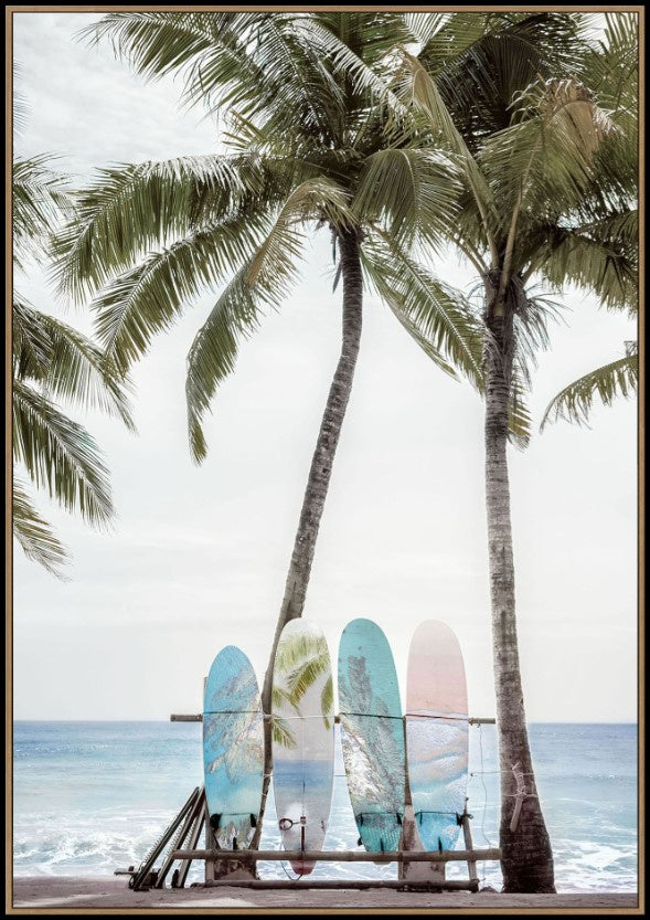 A framed art print depicting a tropical beach scene with three palm trees, ocean waves, and three colorful surfboards resting on a wooden bench in the foreground.