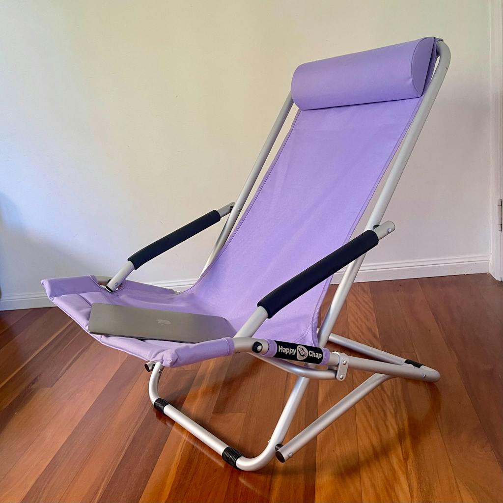 Purple folding beach chair with black armrests on a wooden floor.