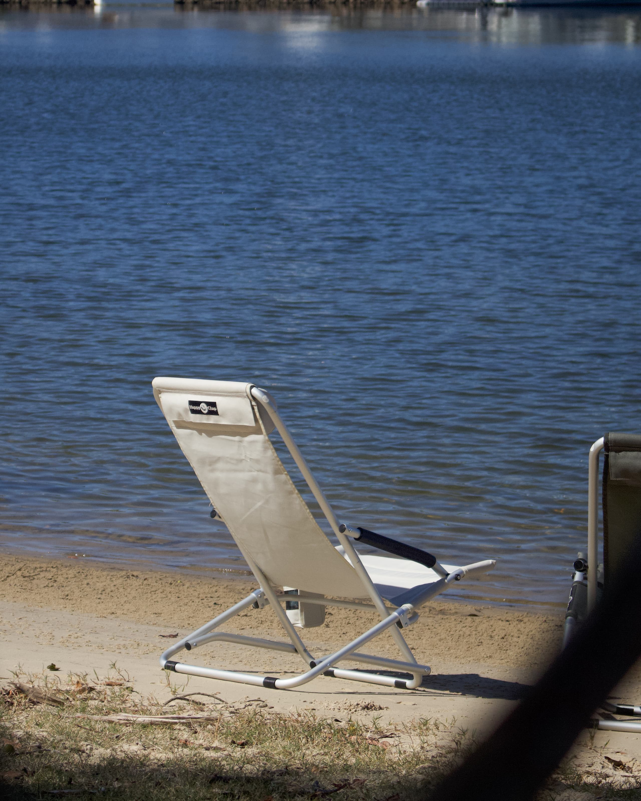 Beige folding chair on a sandy beach with water in the background