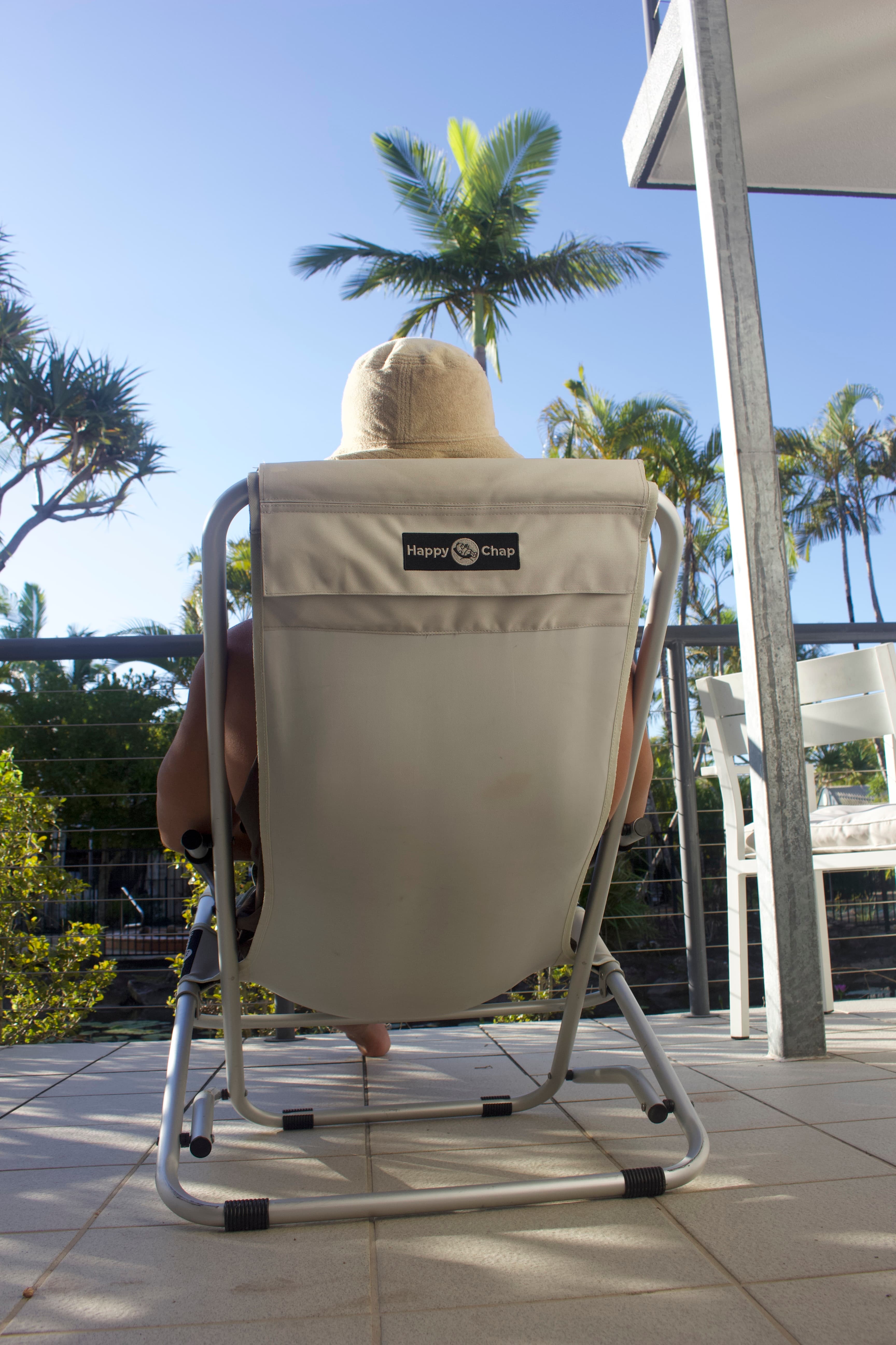 Person sitting in a beige chair with a logo on a patio with palm trees in the background