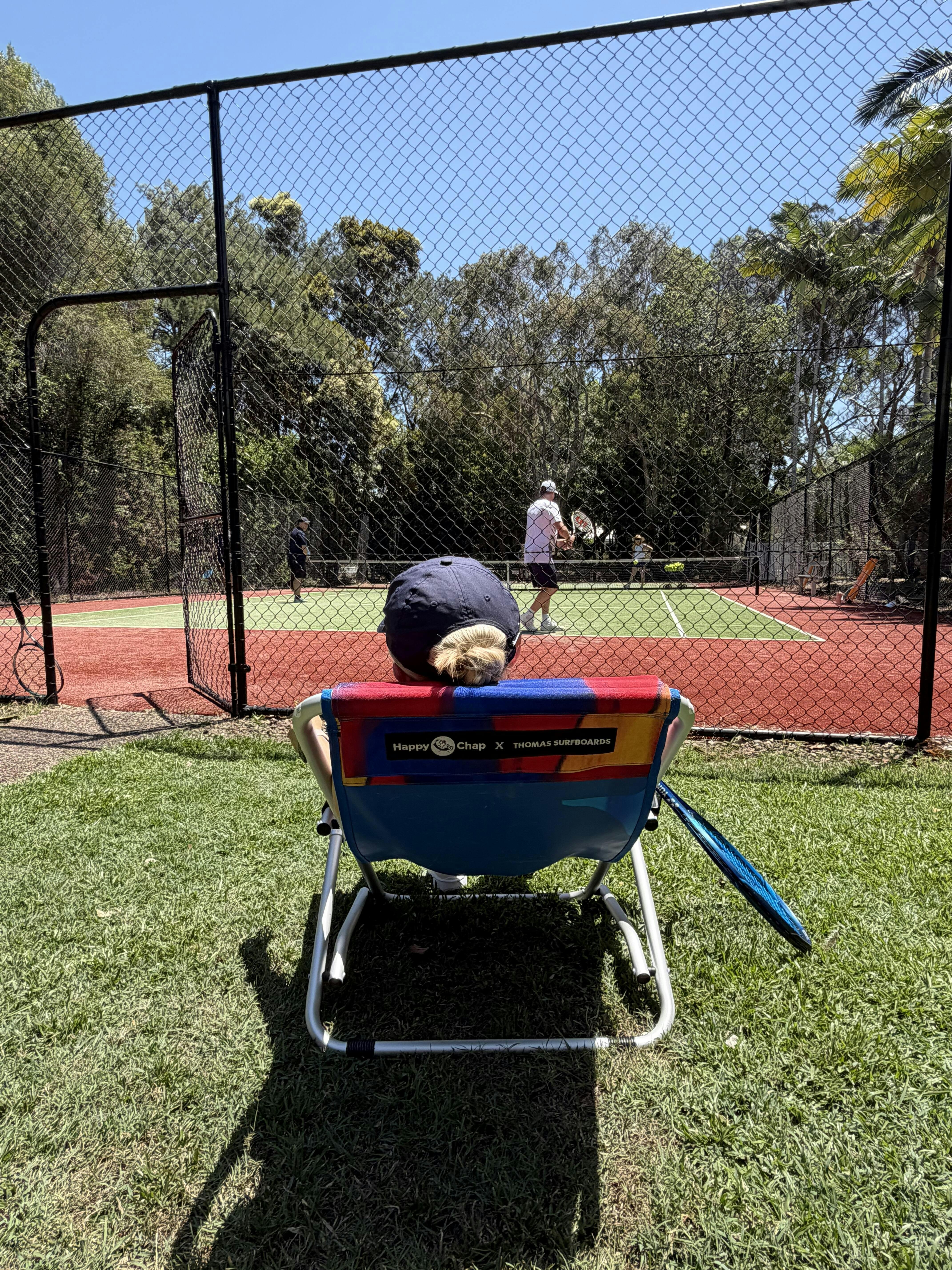 Person sitting on a colorful chair watching tennis on a court