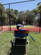 Person sitting on a colorful chair watching tennis on a court