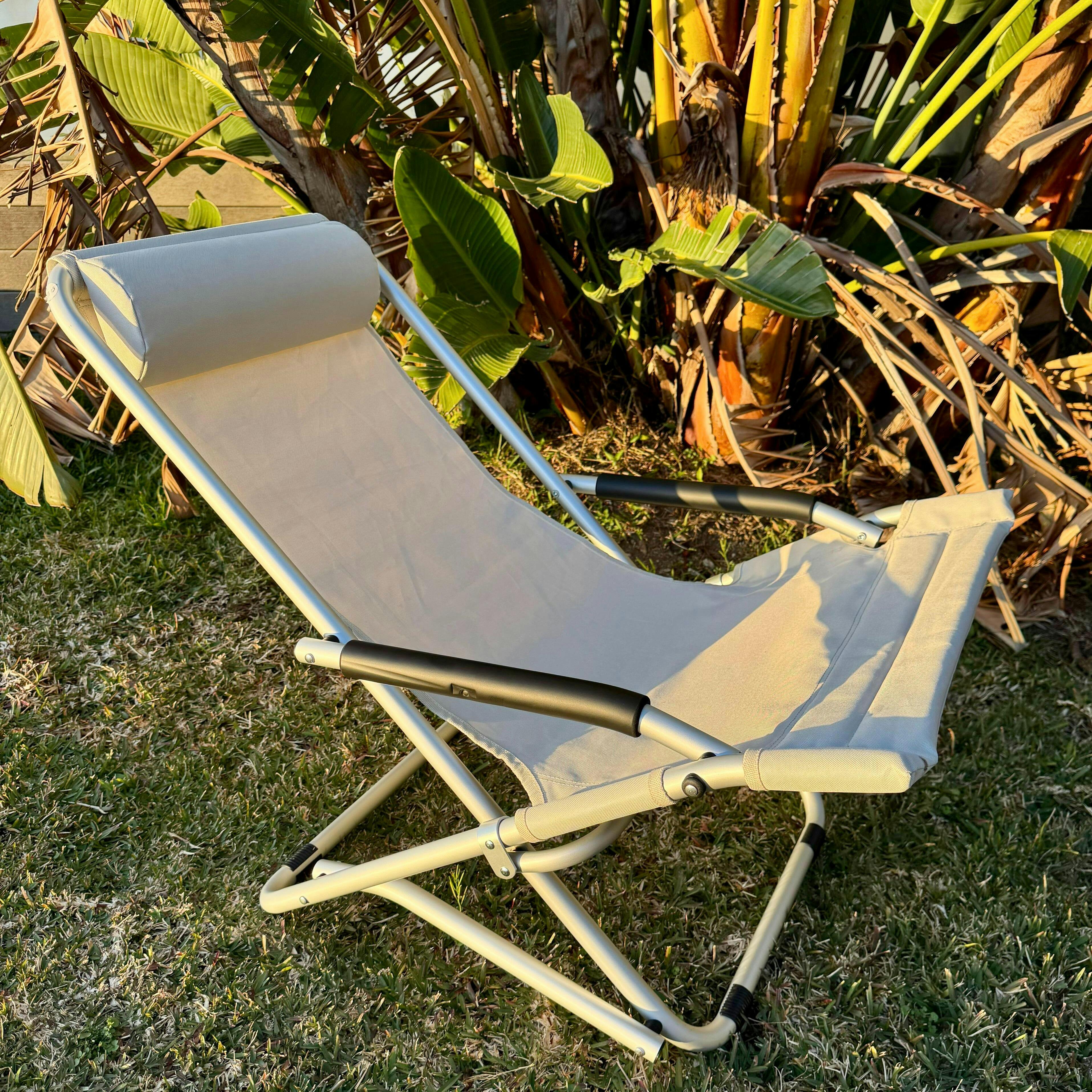 Beige folding lounge chair on grass with plants in the background