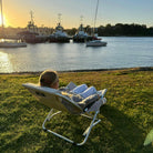 Person sitting in a chair by a waterfront with boats in the background at sunset.