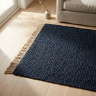Navy blue rug with fringes on a wooden floor in a living room setting.