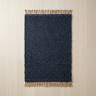 Navy blue rug with beige fringe on a light wood floor