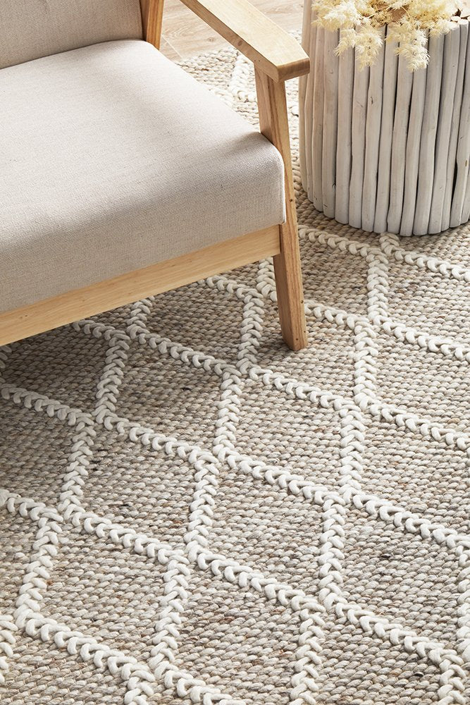 Patterned rug with geometric design on a floor next to a chair and plant.