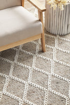 Patterned rug with geometric design on a floor next to a chair and plant.