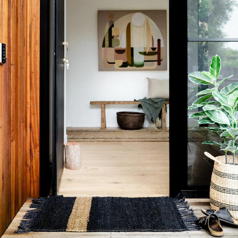 Entryway with a black and gold doormat, wooden bench, and abstract art on the wall.