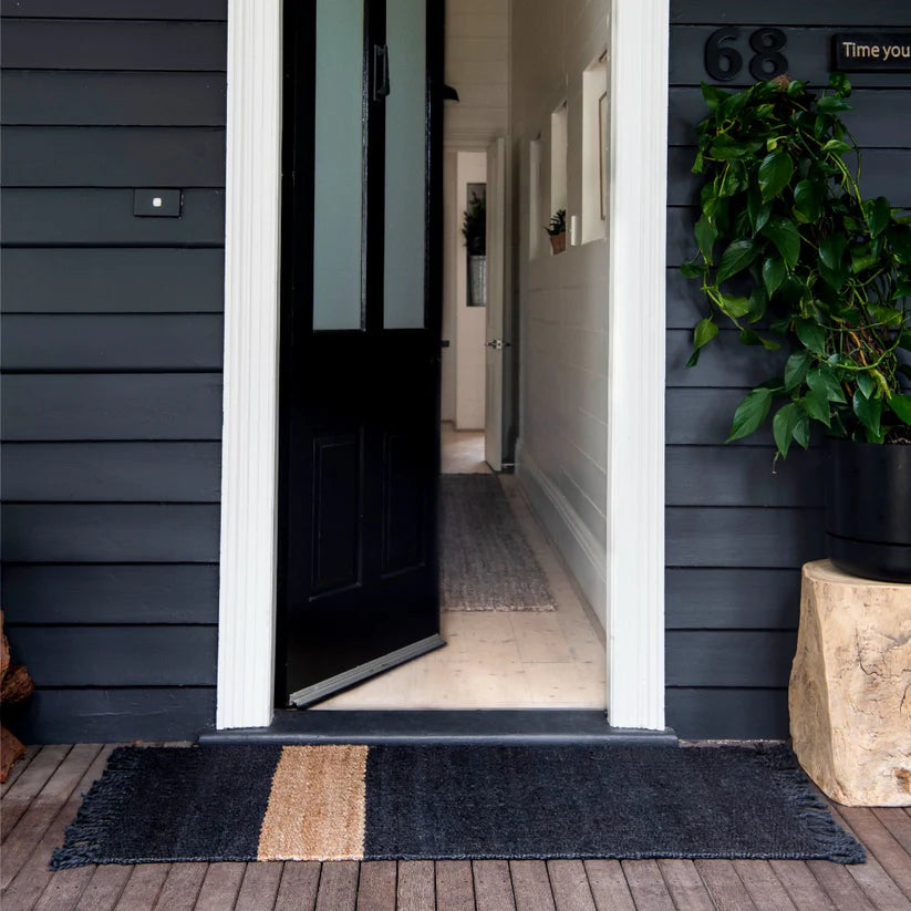 Open door leading into a house with a dark welcome mat on the wooden floor.