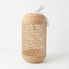 A natural woven rattan or wicker cylindrical lampshade or decorative light fixture with an open geometric pattern, shown on a clean white background. A white cord is visible at the top and a small product tag hangs from the right side.