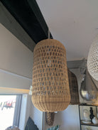 A large cylindrical woven rattan pendant light hanging in a modern room with a white ceiling and dark wooden beams.