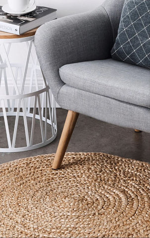 Gray sofa with wooden legs on a textured rug, next to a white side table.