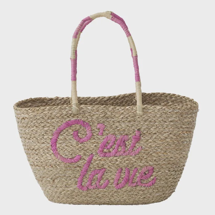 Woven basket with pink handle and 'C'est la vie' text on a light gray background