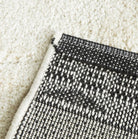 Close-up of a textured black and white rug corner on a beige carpet.