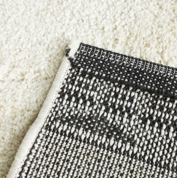 Close-up of a textured black and white rug corner on a beige carpet.