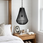 A black beaded pendant light hangs over a wooden nightstand in a bright, modern bedroom with white shiplap walls, a bed with white linens, and decorative items on the table.