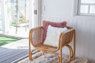 Rattan chair with pink and white sheepskin cushions on a patio with a view of a garden.