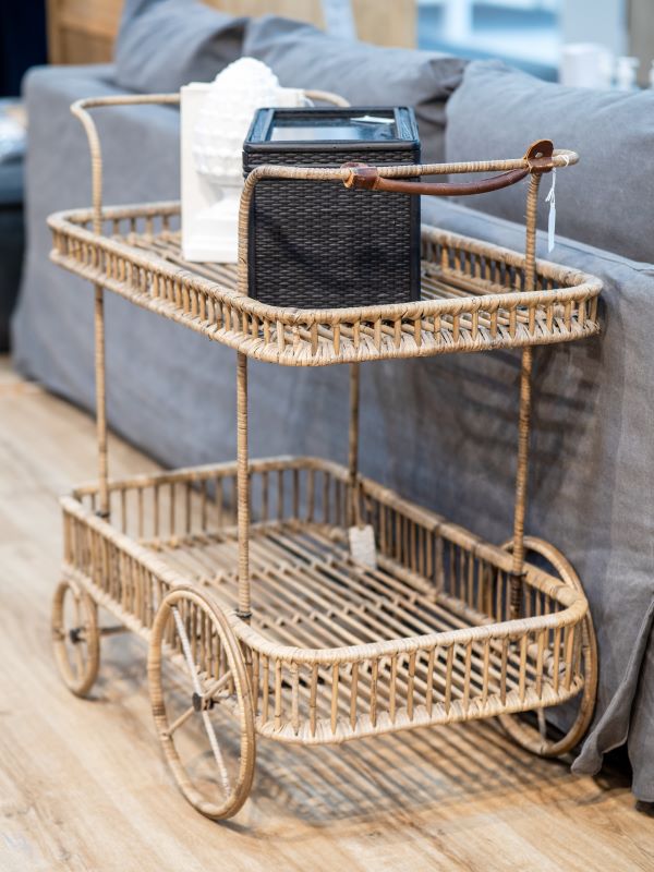 Wicker bar cart with a black lantern and white box on a wooden floor.