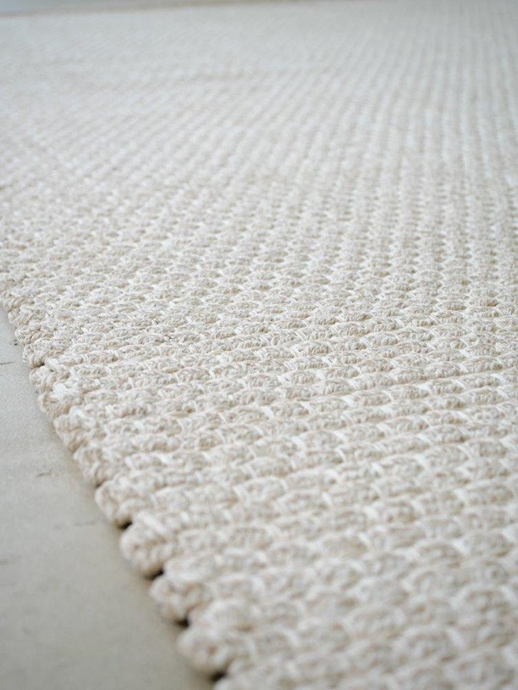 Close-up of a textured white rug on a light gray floor.