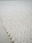 Close-up of a textured white rug on a light gray floor.