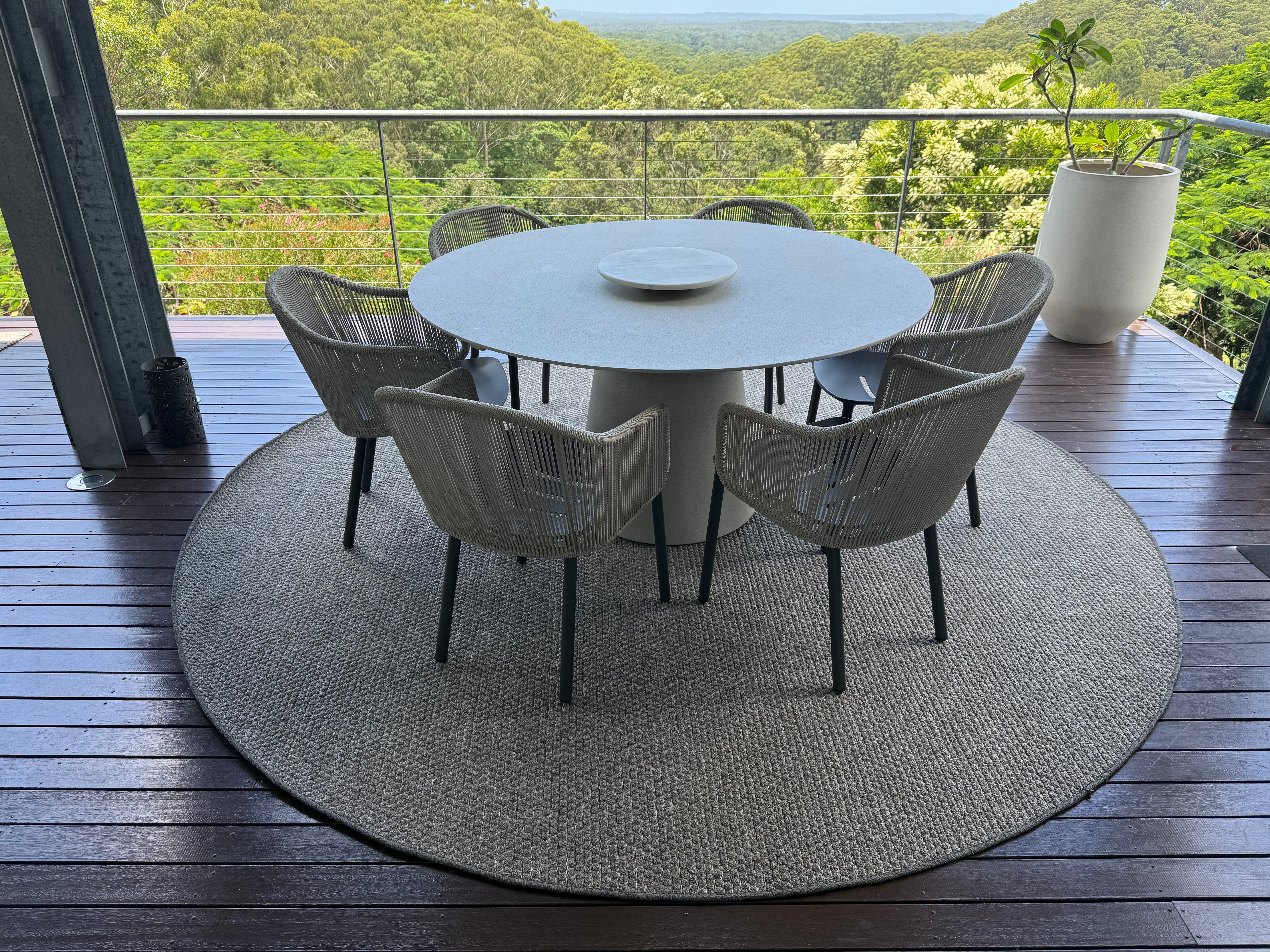 Round dining table with six chairs on a wooden deck overlooking greenery