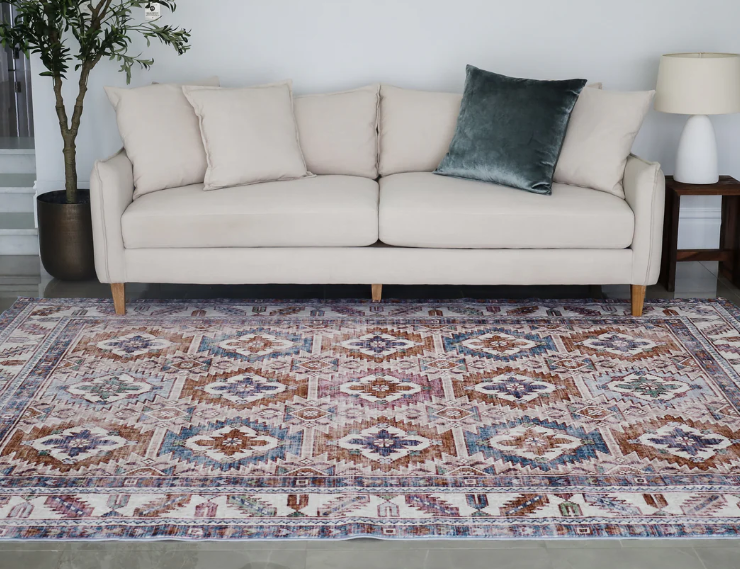 Beige sofa with a decorative pillow on a patterned rug in a living room setting.