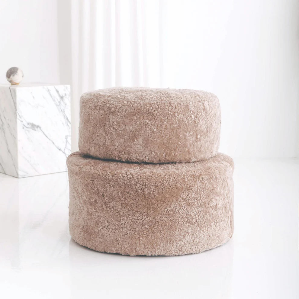 Two fluffy ottomans stacked on a white surface with a light background