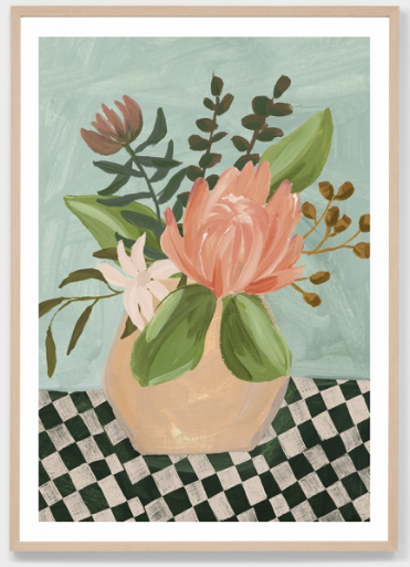 A framed art print featuring a still life painting of a pink protea flower in a beige vase, surrounded by green leaves, set against a light blue-green background with a black and white checkered surface.