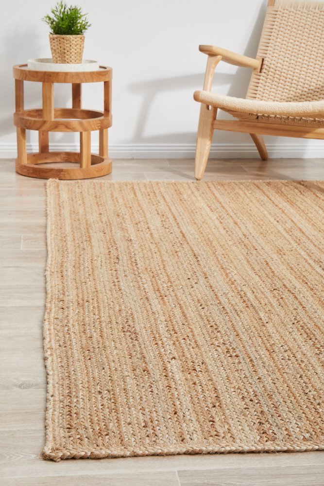 Beige woven rug on a wooden floor with a side table and chair in the background.