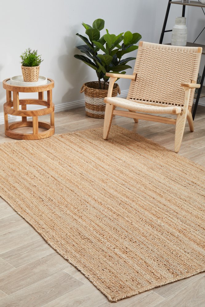 Beige jute rug on a wooden floor with a wicker chair and side table.