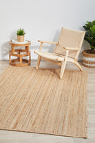 Woven chair and side table on a textured rug with plants in a minimalistic room.