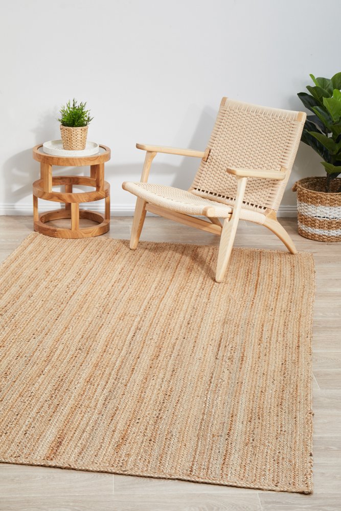 Woven chair and side table on a textured rug with plants in a minimalistic room.