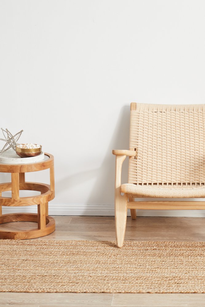Woven chair and side table on a wooden floor with a plain white wall background
