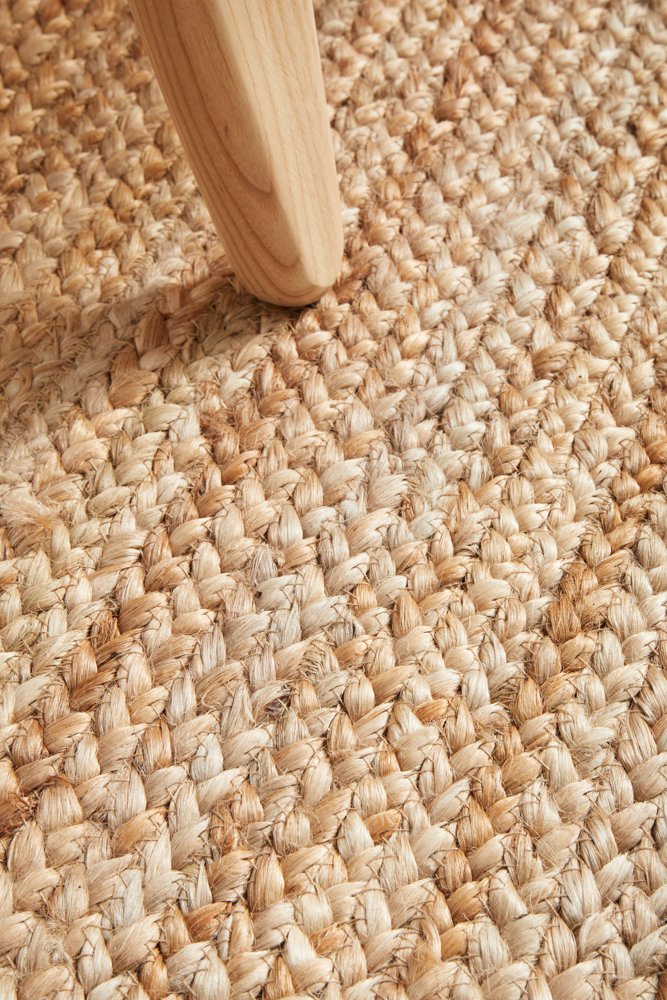 Close-up of textured beige carpet with a wooden furniture leg.