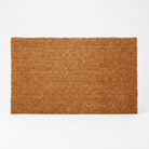 A rectangular natural coir doormat in a warm brown color, shown from a top-down view on a clean white background.