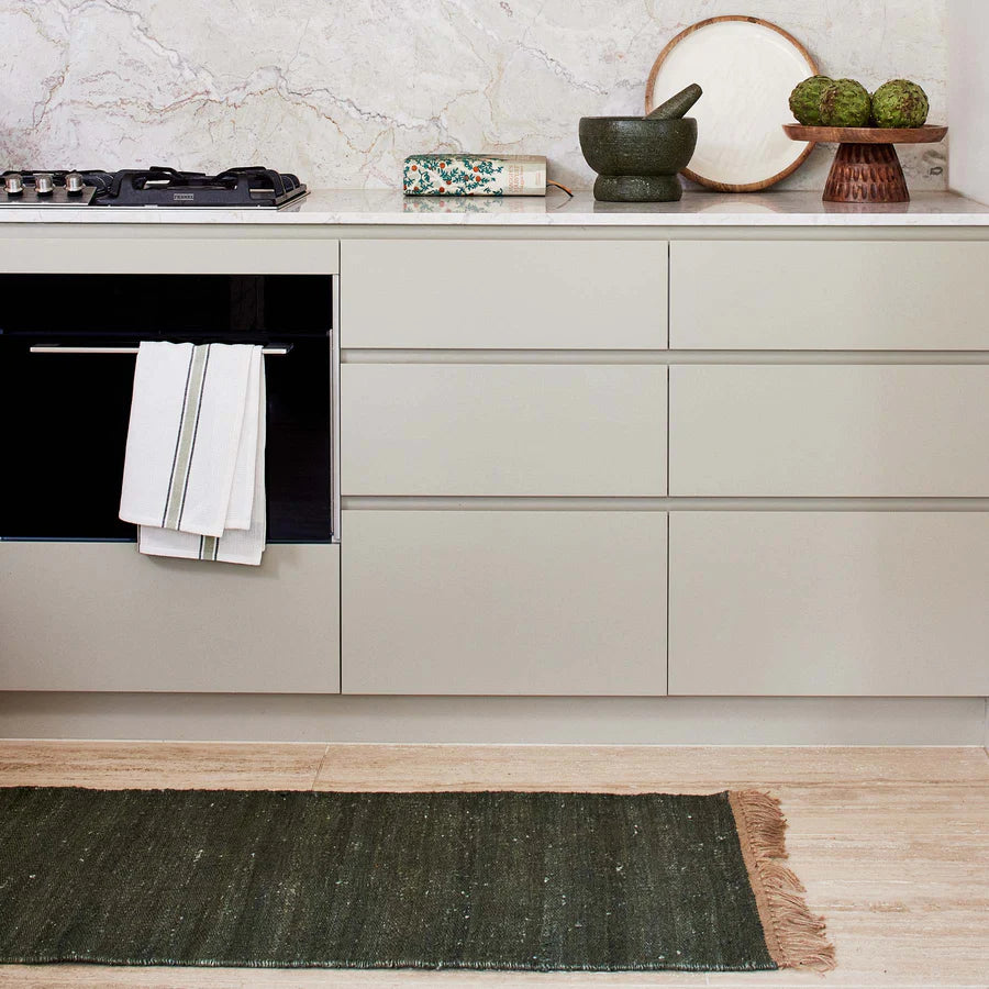 Modern kitchen with light gray cabinets, black oven, and green rug on wooden floor.