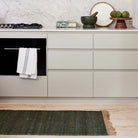 Modern kitchen with light gray cabinets, black oven, and green rug on wooden floor.