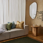 Living room with a beige sofa, decorative pillows, a wooden side table, and a mirror on a wall.