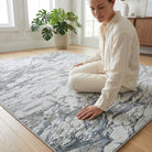 Woman sitting on a textured rug in a room with a plant and wooden furniture.