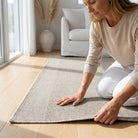 Woman placing a beige rug on a wooden floor in a living room.