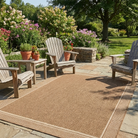 Outdoor patio with wooden chairs and a woven rug in a garden setting